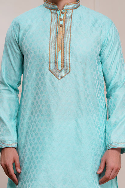 Men's light blue brocade kurta with gold embroidered neckline paired with white churidar, mandarin collar, side pockets, full sleeves - premium Indian formal wear for weddings and special occasions