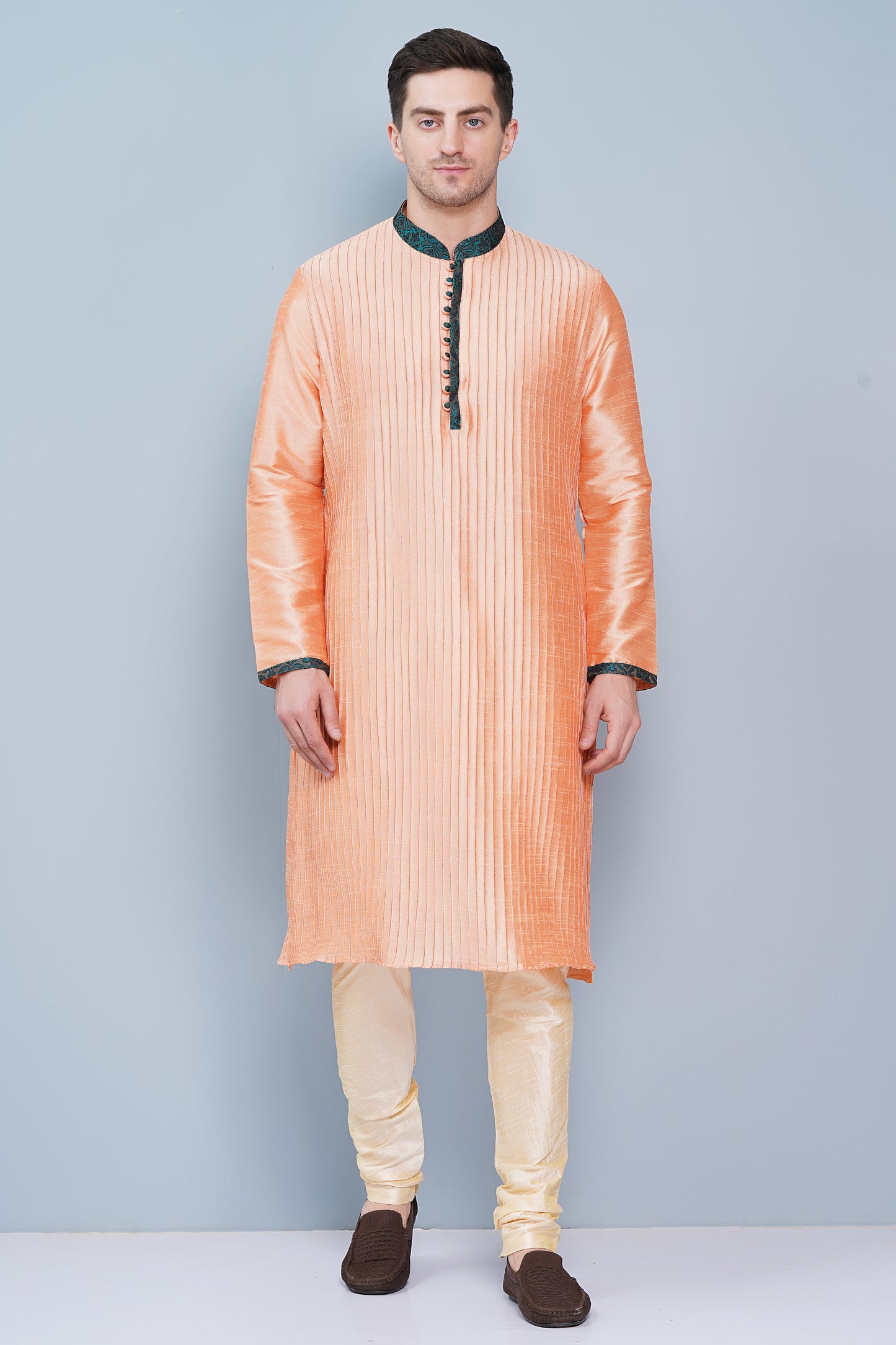 Men Peach color traditional Kurta with green accent  on collar, placket and cuffs, full length, boondi button with loops closure, one fourth placket, full sleeves, mandarin collar, side pockets on Kurta with Off-white or cream color chudidar pajama. Perfect traditional wear for family special occasions, wedding, house warming, casual wear