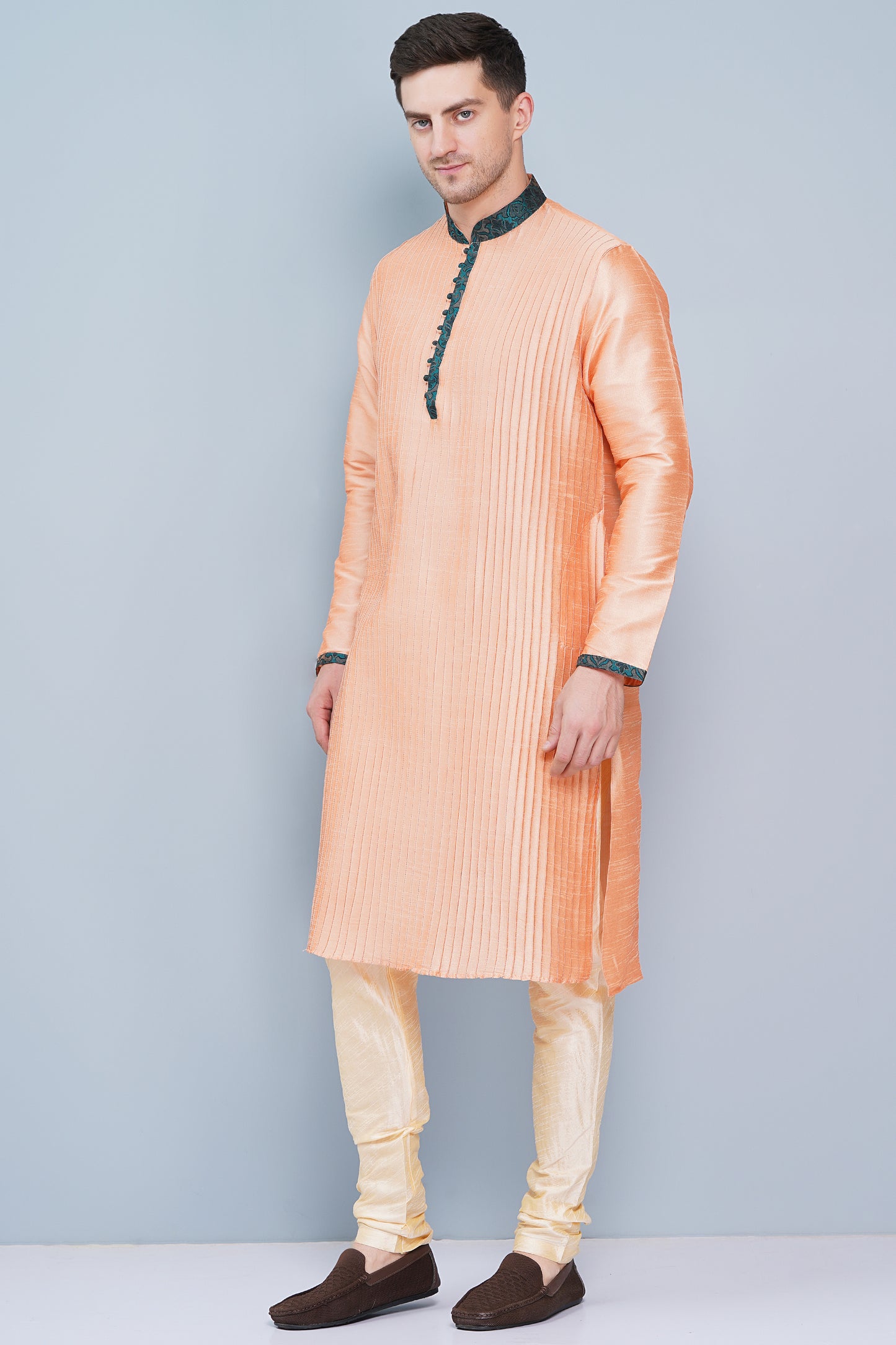 Men Peach color traditional Kurta with green accent  on collar, placket and cuffs, full length, boondi button with loops closure, one fourth placket, full sleeves, mandarin collar, side pockets on Kurta with Off-white or cream color chudidar pajama. Perfect traditional wear for family special occasions, wedding, house warming, casual wear