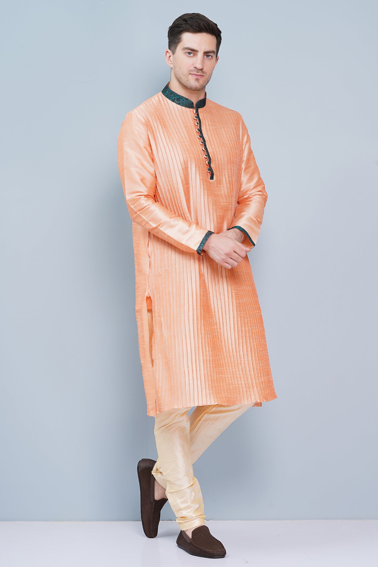 Men Peach color traditional Kurta with green accent  on collar, placket and cuffs, full length, boondi button with loops closure, one fourth placket, full sleeves, mandarin collar, side pockets on Kurta with Off-white or cream color chudidar pajama. Perfect traditional wear for family special occasions, wedding, house warming, casual wear