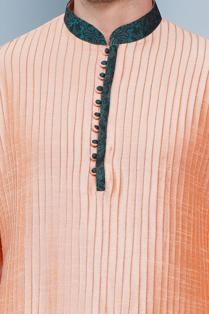 Men Peach color traditional Kurta with green accent  on collar, placket and cuffs, full length, boondi button with loops closure, one fourth placket, full sleeves, mandarin collar, side pockets on Kurta with Off-white or cream color chudidar pajama. Perfect traditional wear for family special occasions, wedding, house warming, casual wear